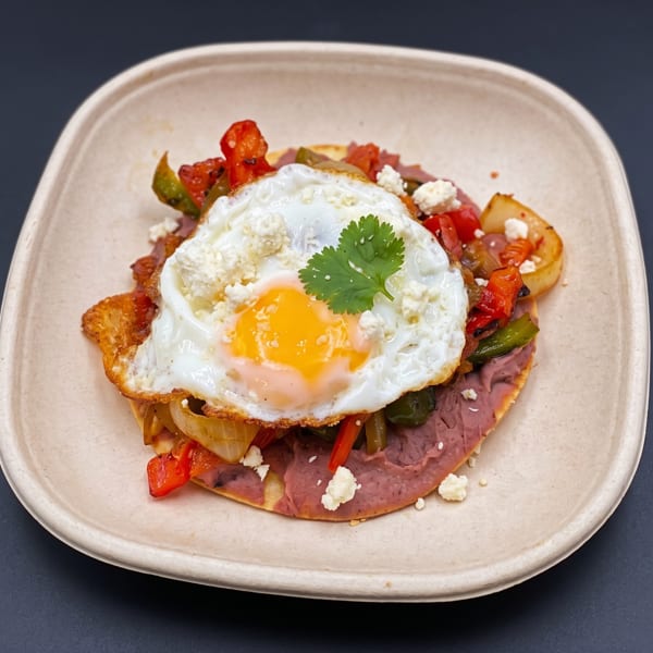 A fried egg atop a tortilla with refried beans, sautéed peppers, onions, and crumbled cheese.