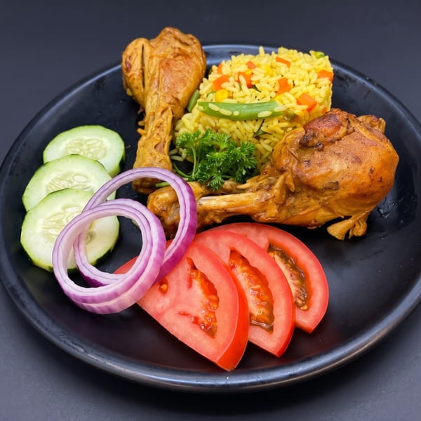 Two chicken drumsticks with yellow vegetable rice, sliced cucumber, tomato, and red onion on a black plate.