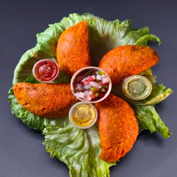 Bright orange empanadas on lettuce, served with various dipping sauces and pico de gallo.
