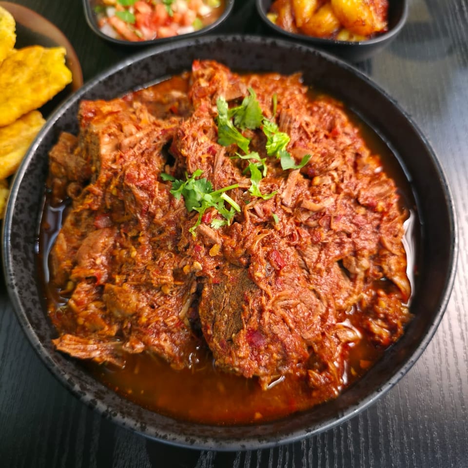 Stewed shredded beef in red sauce with tostones, sweet plantains, and pico de gallo.
