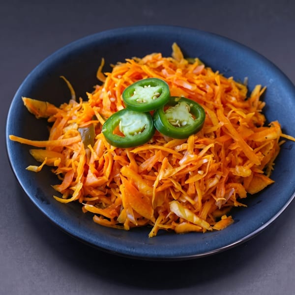 Shredded orange salad with three green jalapeño slices on top, in a dark blue bowl.